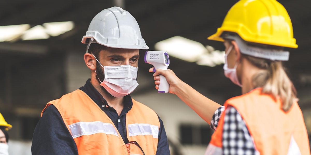 worker in hardhat taking the temperature of another worker
